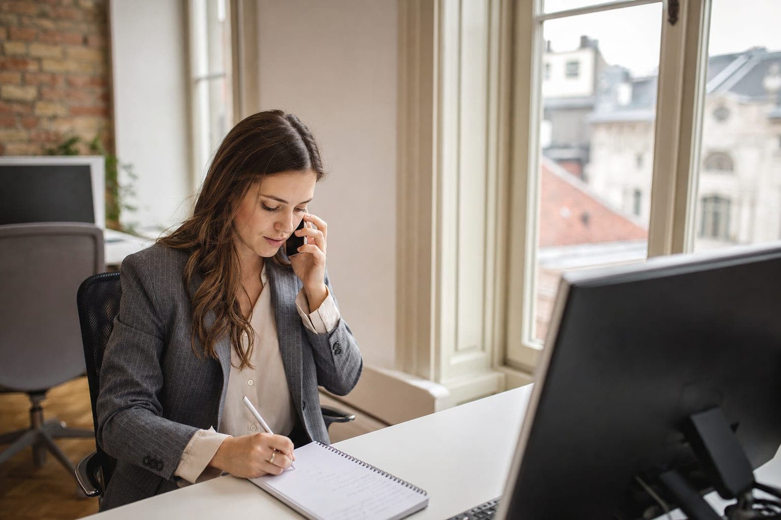 Recruiterin im Telefonat mit Notizblock am Schreibtisch